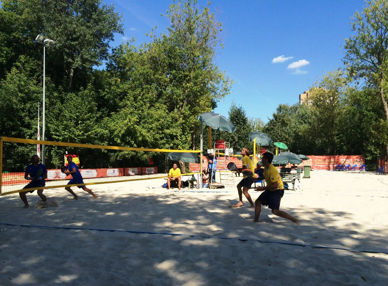 Jogadores de beach tennis disputam uma partida na areia com rede e raquetes.